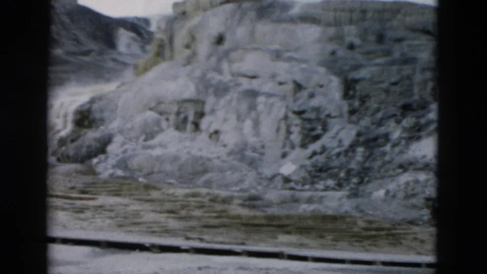 Yellowstone home-movie still showing layered pale terrace formations and a flat wet foreground, with soft 8mm color and grain.