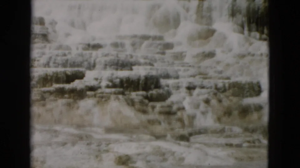 Yellowstone 8mm still showing a brighter terrace section with horizontal mineral shelves, darker deposits, and wet lower ground.