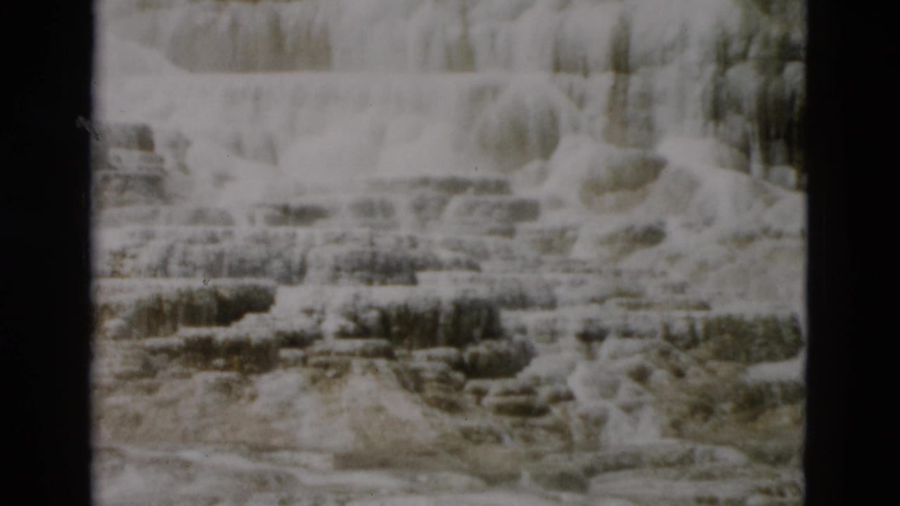 Pale terraced rock formations with mineral ledges and dark film borders.