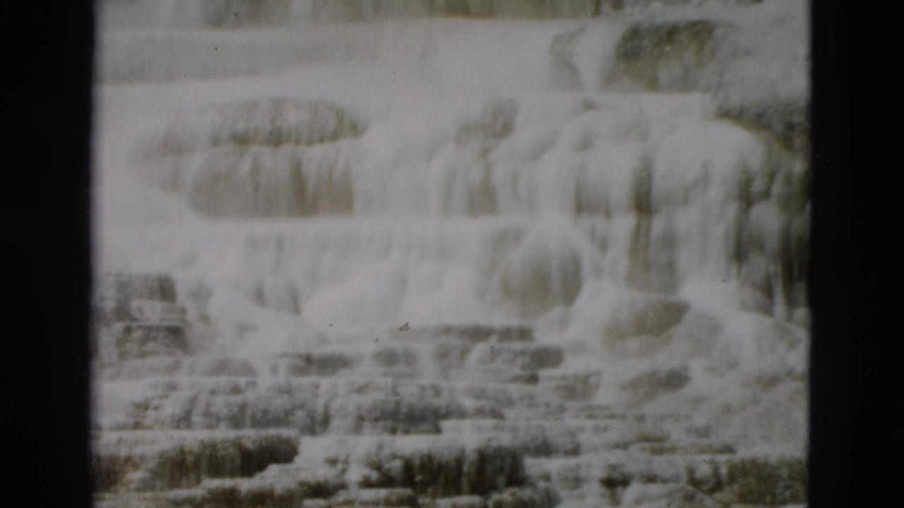 1958 Yellowstone home-movie frame with layered mineral terraces, soft exposure, and visible film gate edges.