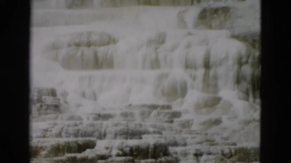 1958 Yellowstone home-movie frame with layered mineral terraces, soft exposure, and visible film gate edges.