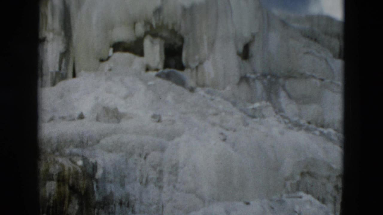 Yellowstone 8mm frame with a dark rock opening surrounded by thick ice, snow mounds, and vertical icicles.