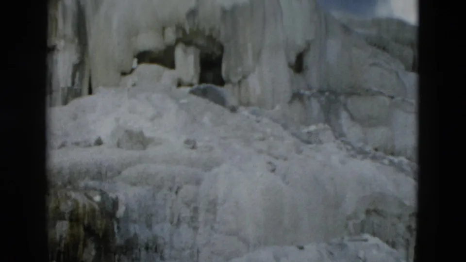 Yellowstone 8mm frame with a dark rock opening surrounded by thick ice, snow mounds, and vertical icicles.
