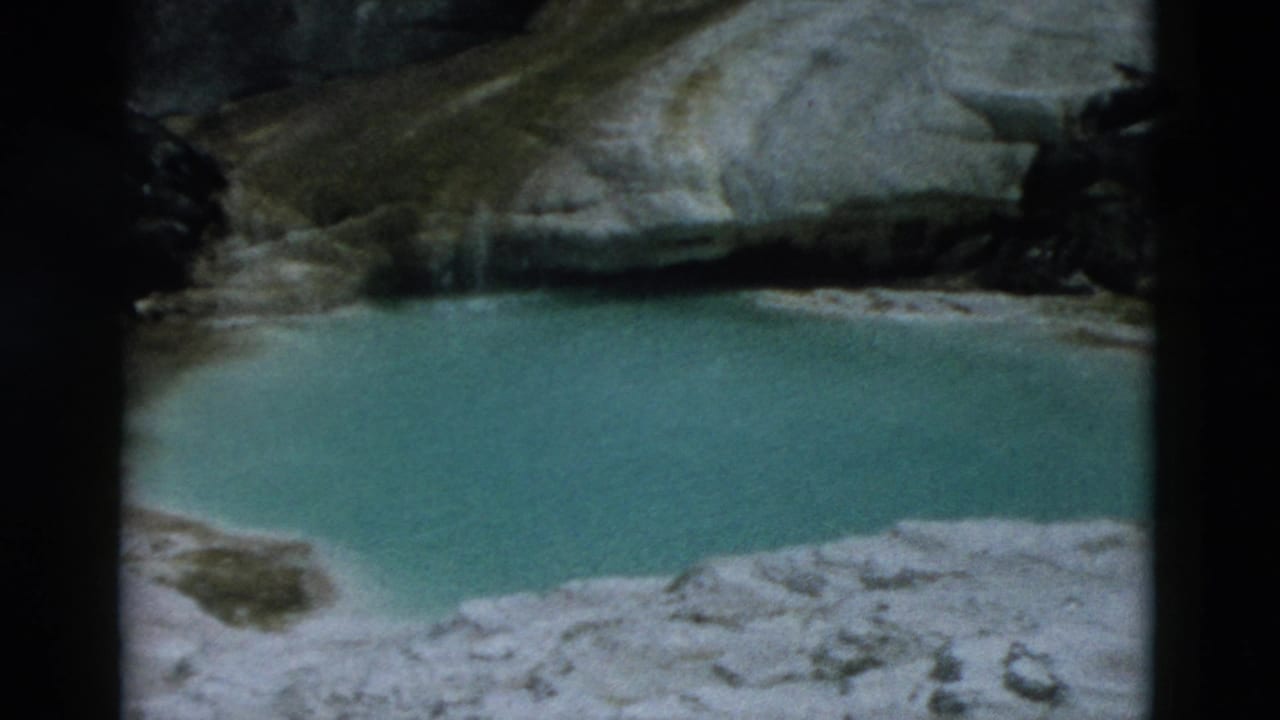 Turquoise spring water beside pale rock and mineral deposits.