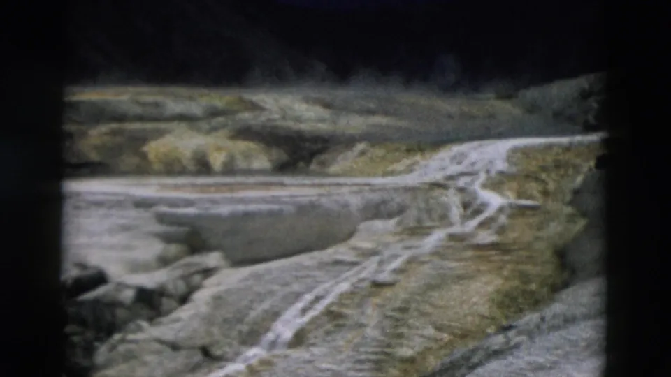 1958 Yellowstone 8mm frame showing pale mineral channels running through a rocky terrace landscape near geothermal water.