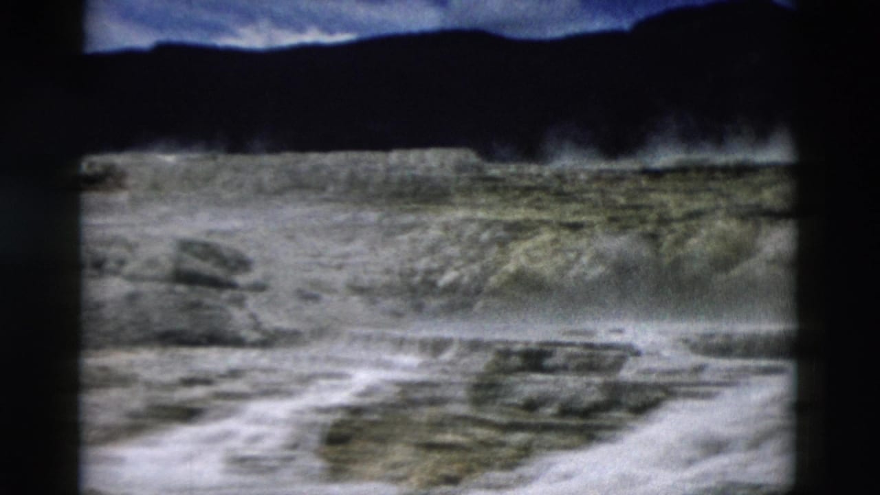 1958 Yellowstone 8mm frame showing steaming geothermal terraces with dark hills in the background.