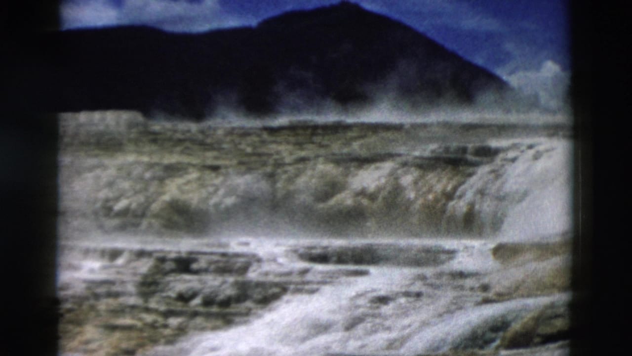 Yellowstone geothermal landscape with pale mineral terraces, drifting steam, and dark hills in a 1958 8mm frame.