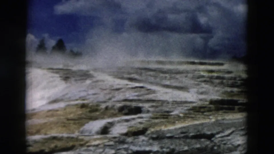 1958 Yellowstone 8mm frame showing pale geothermal terraces, steam drifting across the basin, and a moody overcast sky.