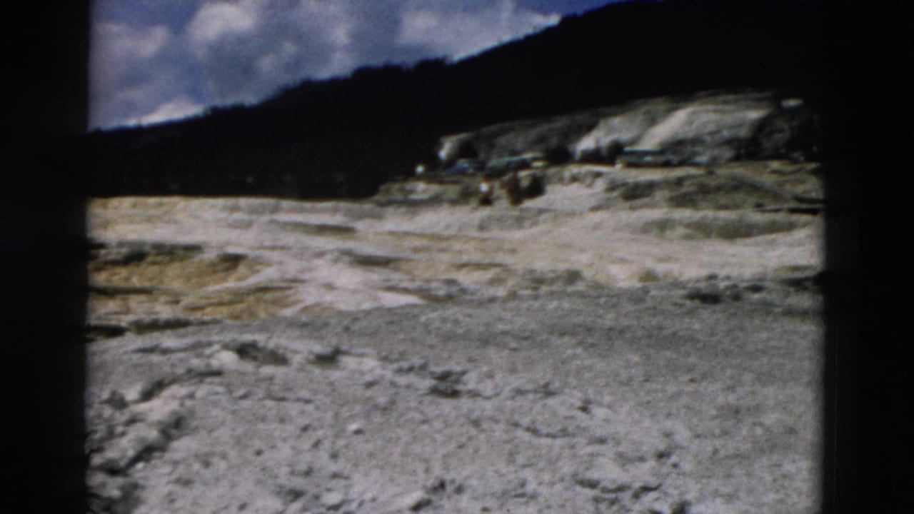 Rocky open ground and wooded hillside seen through dark 8mm frame borders.