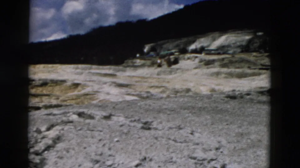 1958 Yellowstone landscape frame with pale mineral-looking ground, low hills, clouds, and heavy film gate shadowing.