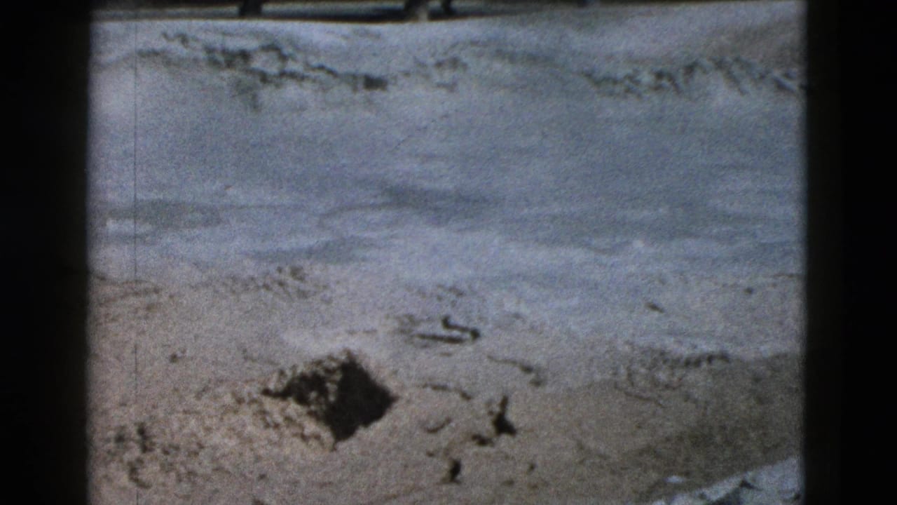 Roadside sand or pale pavement detail in the Yellowstone 1958 home-movie clip, framed by dark 8mm film edges.
