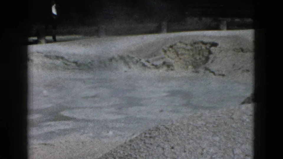 1958 Yellowstone frame with pale mineral terrain, scattered rock deposits, dark border shadows, and a small distant visitor near the top.