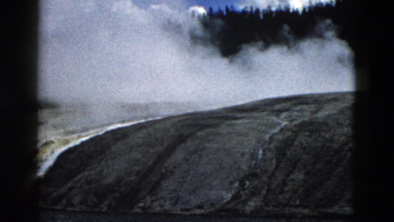 Steam rises behind a rocky mineral hillside with a dark forest line above.
