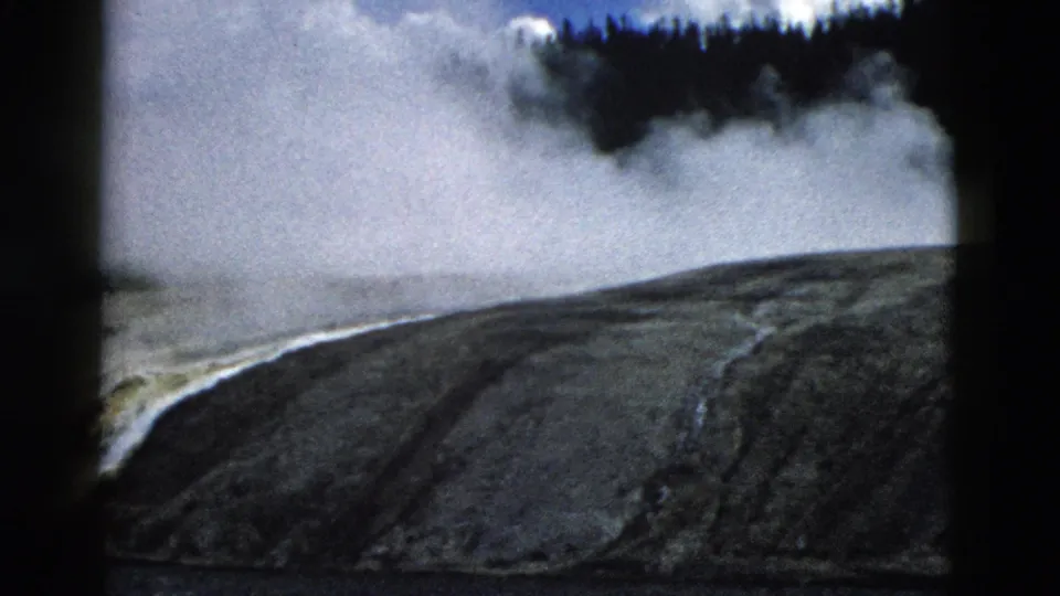1958 Yellowstone 8mm frame showing steam drifting behind a barren mineral-streaked slope and dark forest edge.