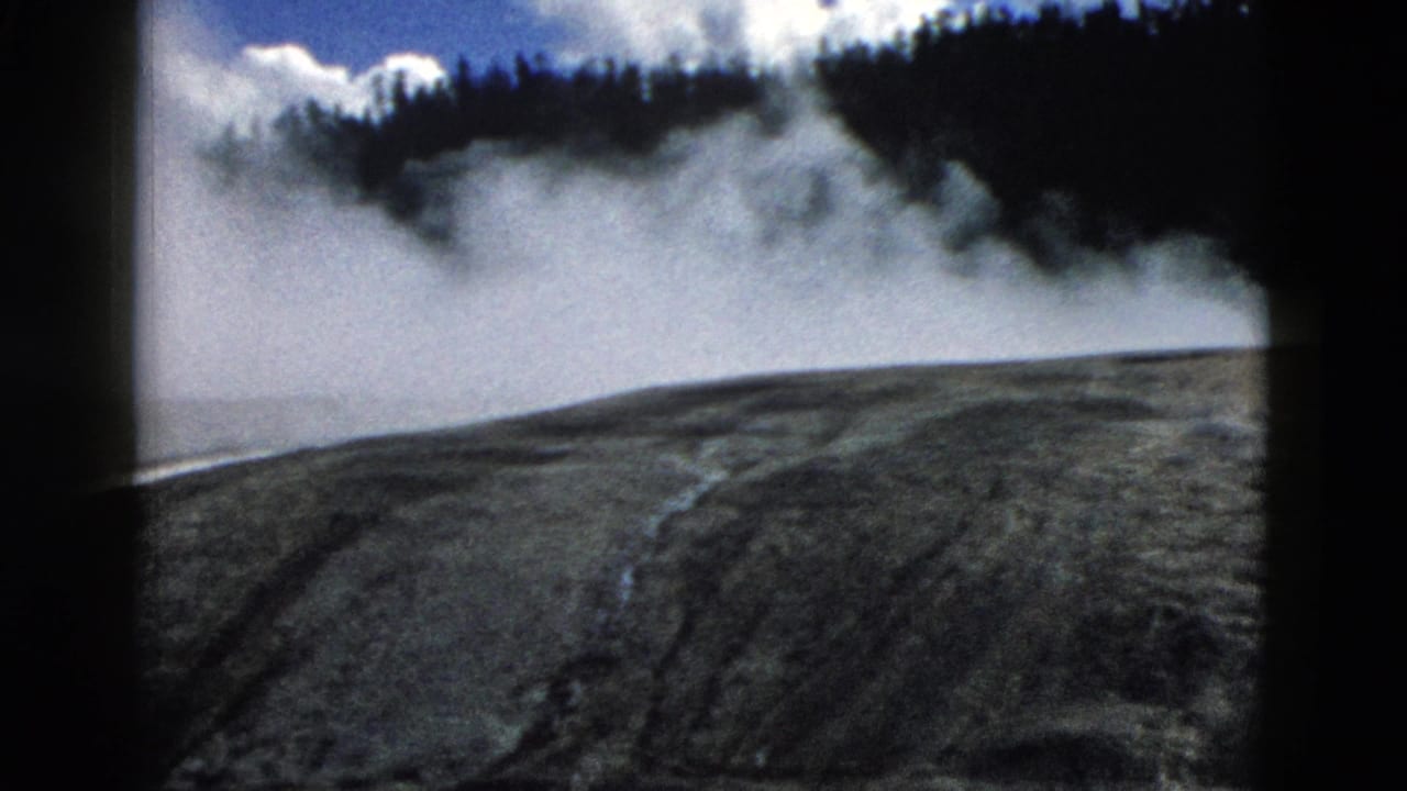 A broad mineral slope sits below drifting steam and a forested ridge.