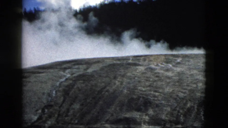 Yellowstone 1958 8mm still showing thick white steam over mineral-streaked ground with dense forest in the background.