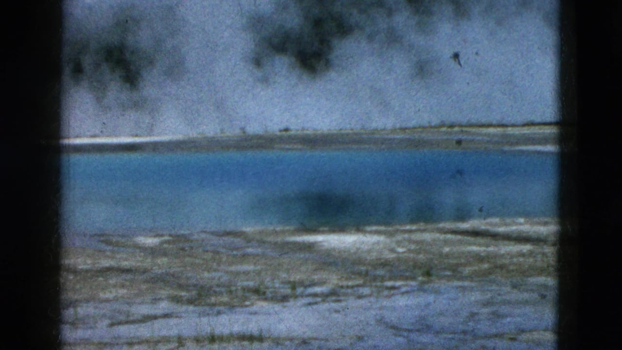 Turquoise geothermal water with steam rising behind a pale shoreline.
