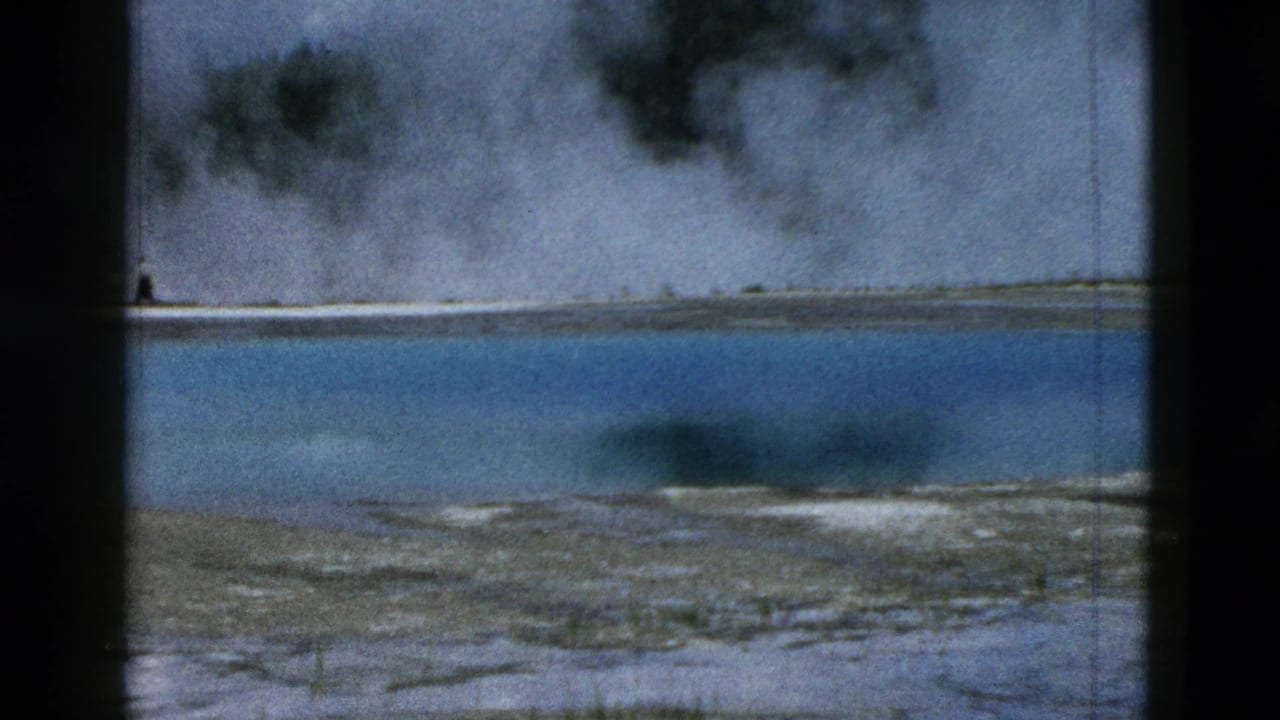 1958 Yellowstone frame looking across blue geothermal water toward steam and a pale opposite shore.