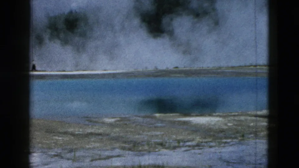 1958 Yellowstone frame looking across blue geothermal water toward steam and a pale opposite shore.