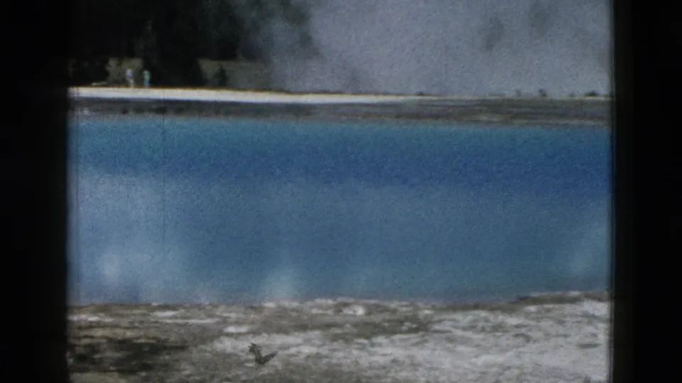 1958 Yellowstone home-movie view of a broad blue hot spring, low steam, pale mineral deposits, and small distant visitors at the edge.