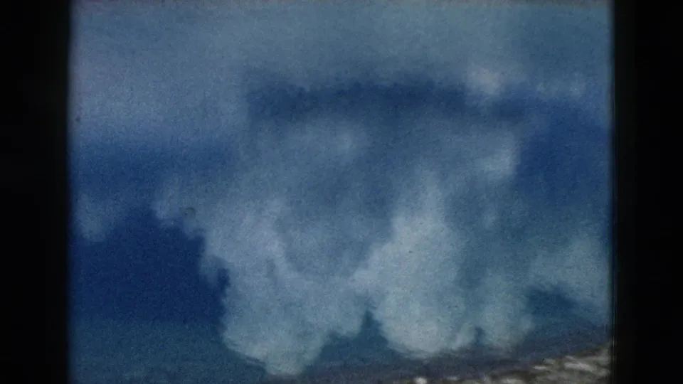 1958 Yellowstone home-movie frame of broad cloud reflections in blue lake water, softened by 8mm grain and focus.
