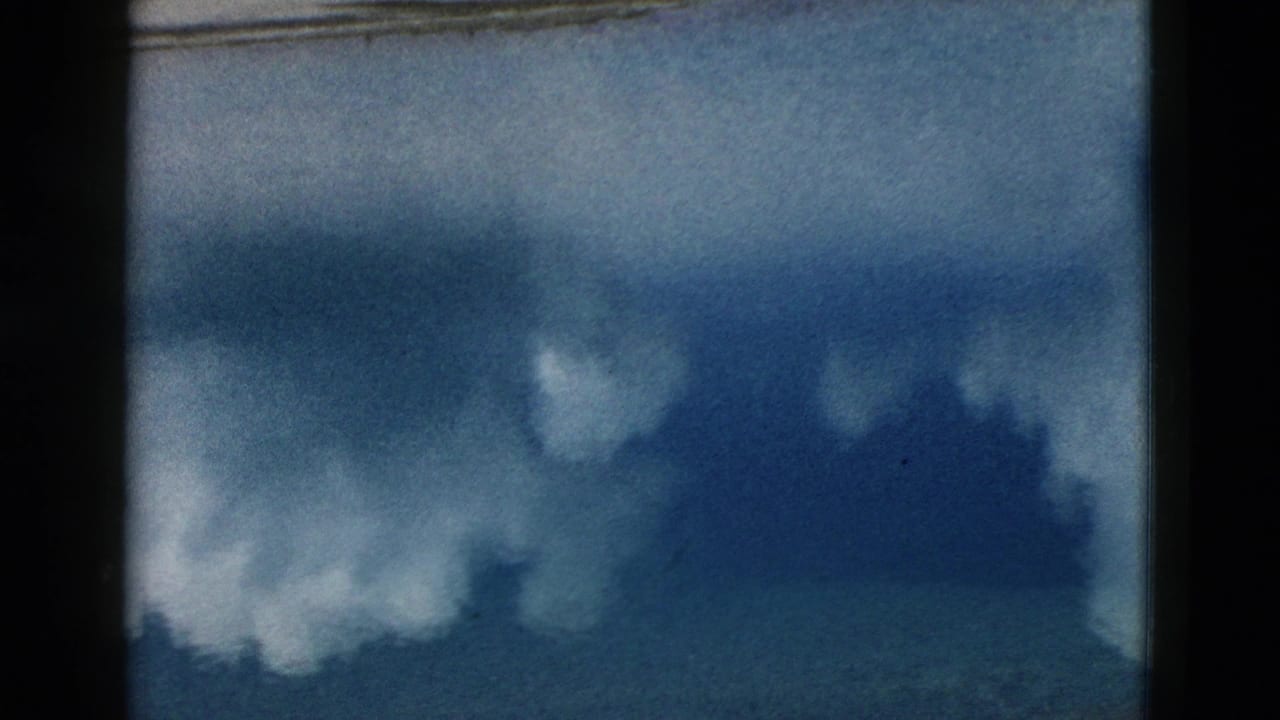 Blue-toned smoke or steam rising above a dark horizon under cloudy sky.
