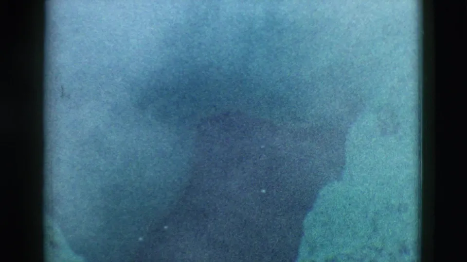 1958 Yellowstone home-movie frame showing a soft blue landscape with a dark smoke or steam shape and pale reflection.