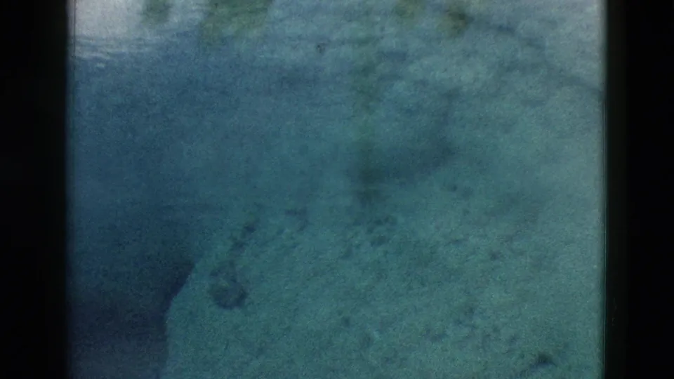 1958 Yellowstone 8mm frame showing murky blue-green spring water, pale rock surfaces, and darker forms beneath the surface.