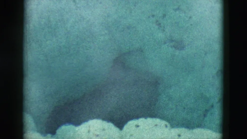 1958 Yellowstone 8mm frame showing a pale foreground ledge, cloudy water, and darker submerged contours in a spring.