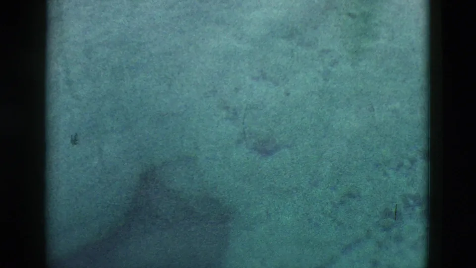 1958 Yellowstone 8mm frame of murky spring water with faint rock textures, sediment, and darker underwater shadows.