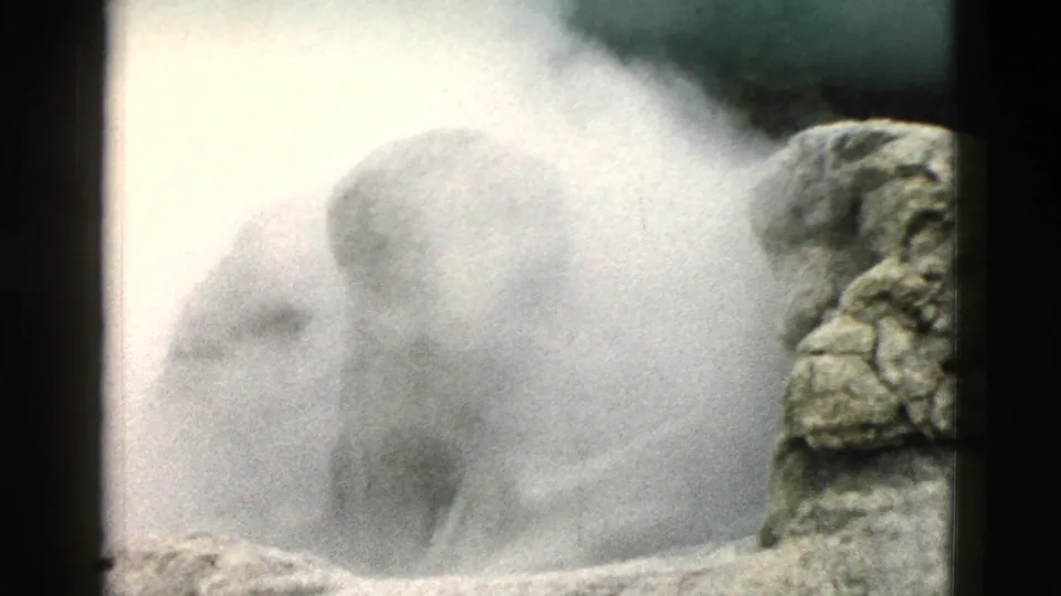 White geothermal steam rises around rough rock in Yellowstone, with a dark vent area and visible 8mm film grain.