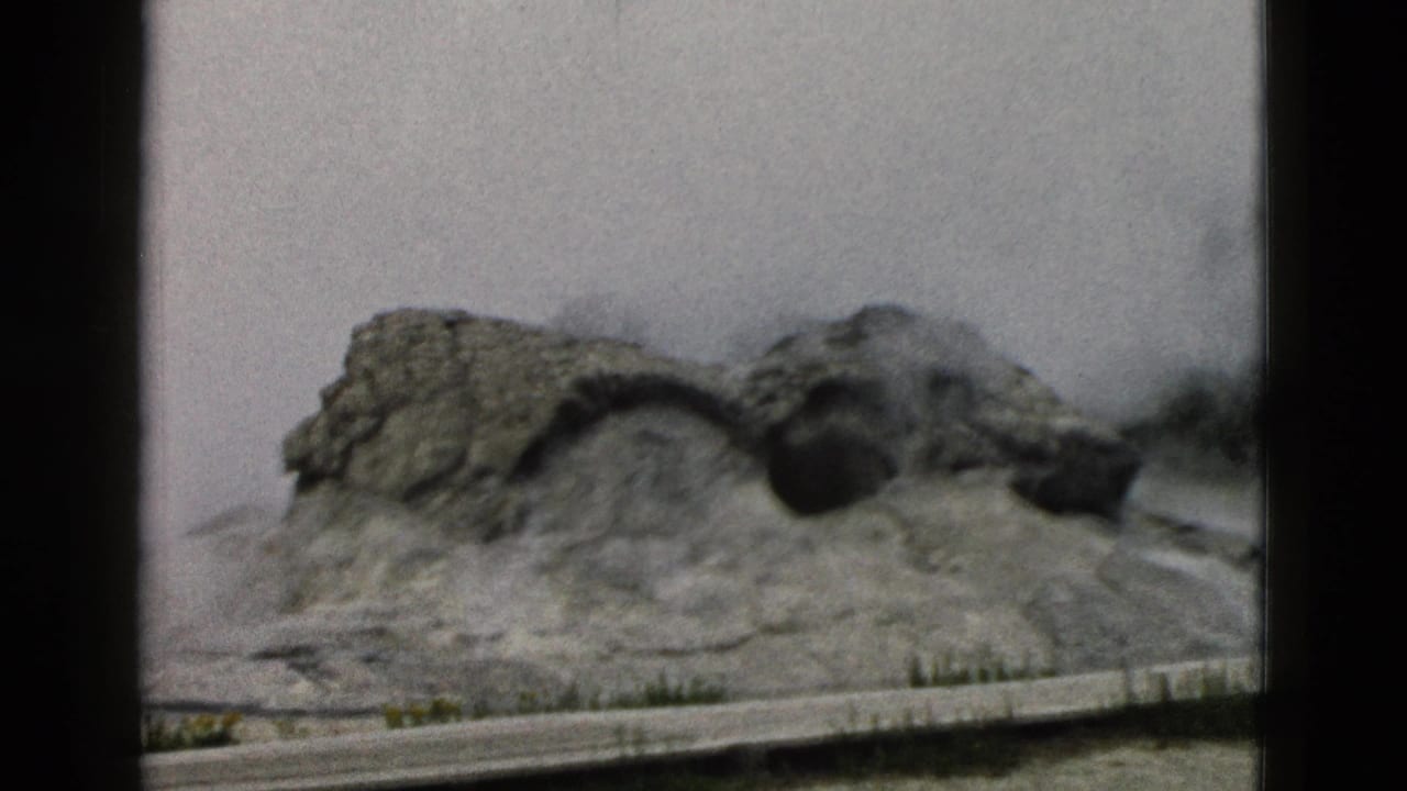 Steam rising from the Old Faithful geyser mound behind a low viewing barrier.