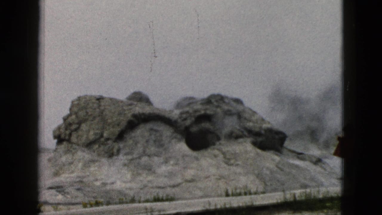1958 Yellowstone frame of the Old Faithful geyser mound with steam building under a pale sky.