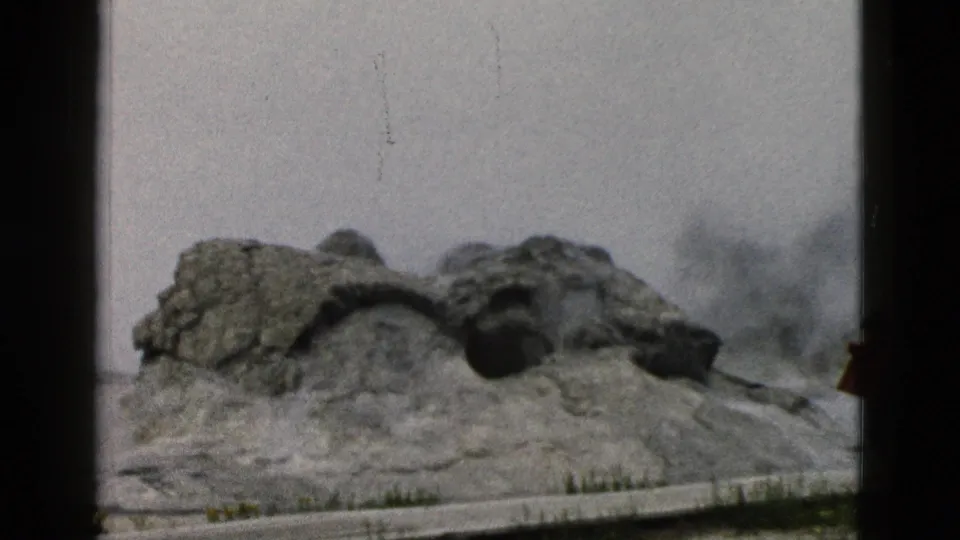1958 Yellowstone frame of the Old Faithful geyser mound with steam building under a pale sky.