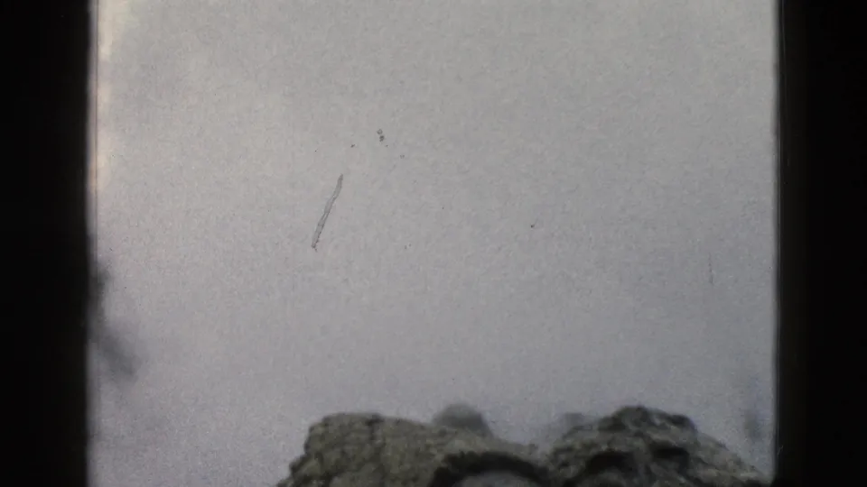1958 Yellowstone home-movie frame with the geyser mound low in view and steam spreading across the sky.