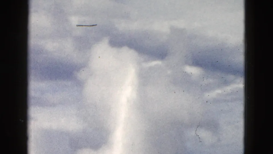 1958 Yellowstone 8mm frame with a white geyser plume drifting below layered gray clouds and visible film wear.