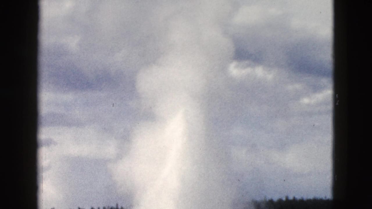 Old Faithful's steam and water plume expands against a blue-gray cloudy sky in this 1958 Yellowstone 8mm home-movie frame.