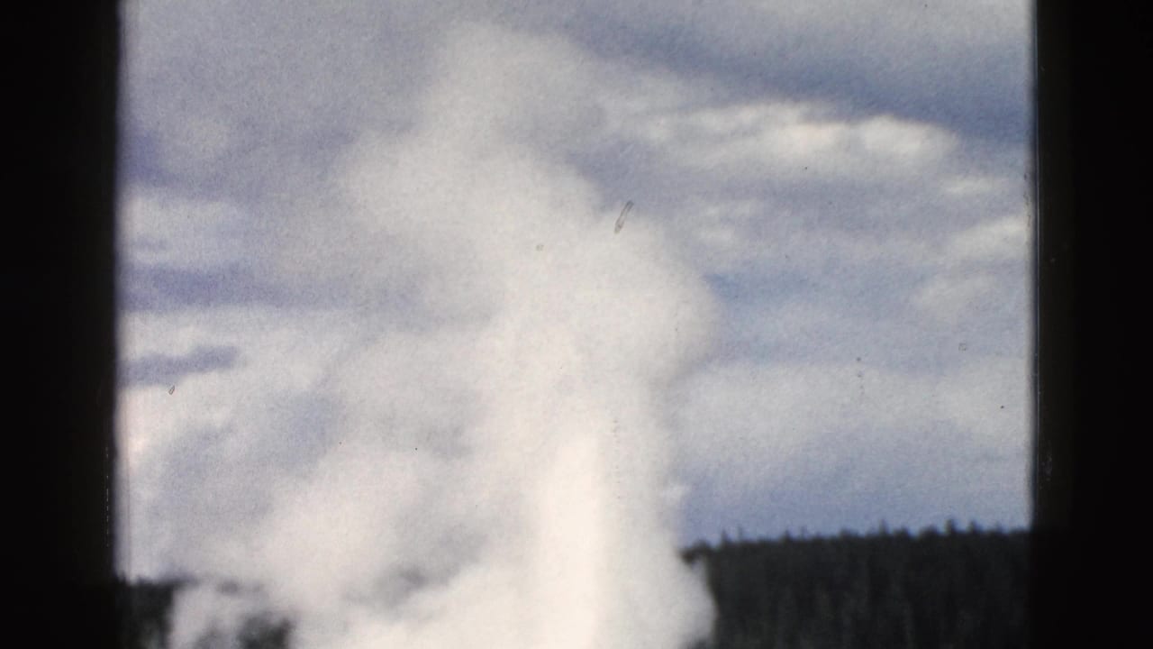 Old Faithful's steam plume rises behind dark film-frame borders and evergreen forest.