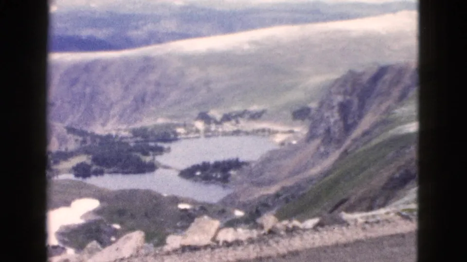 A late clip frame shows a broad Yellowstone mountain basin with lakes, pale snow patches, green slopes, and rocky foreground detail.