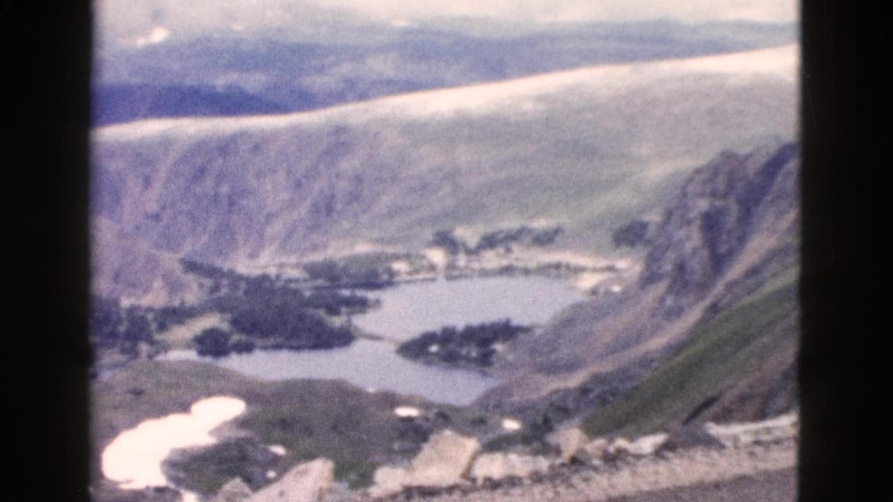Mountain canyon overlook with lake, snow patches, slopes, cloudy sky, and 8mm frame borders.