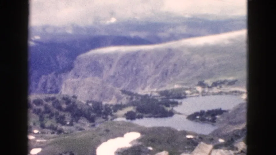 1958 Yellowstone home-movie frame showing canyon walls, a lake edge, trees, snow patches, and muted 8mm color.