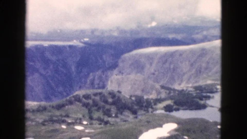 Yellowstone canyon and lake terrain in a 1958 8mm frame, with trees below, snow patches, and faded color.