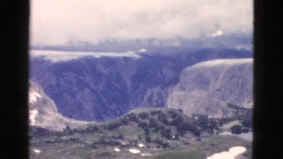1958 8mm Yellowstone panorama ending on canyon walls, distant water, wooded ridge, snow, and cloudy sky.