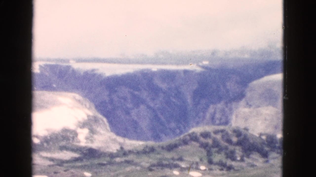 Wide valley view with pale snow, rounded ridges, dark cliff walls, and soft 8mm color shift.