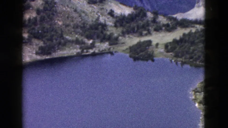 Yellowstone-area 8mm frame with a broad lake, evergreen shoreline, and rugged mountain terrain in faded blue-purple color.