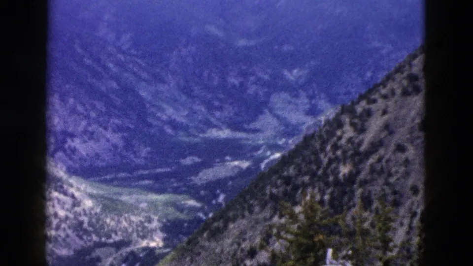Faded 8mm Yellowstone frame showing a broad mountain valley, ridged slopes, scattered trees, and a rocky foreground hillside.