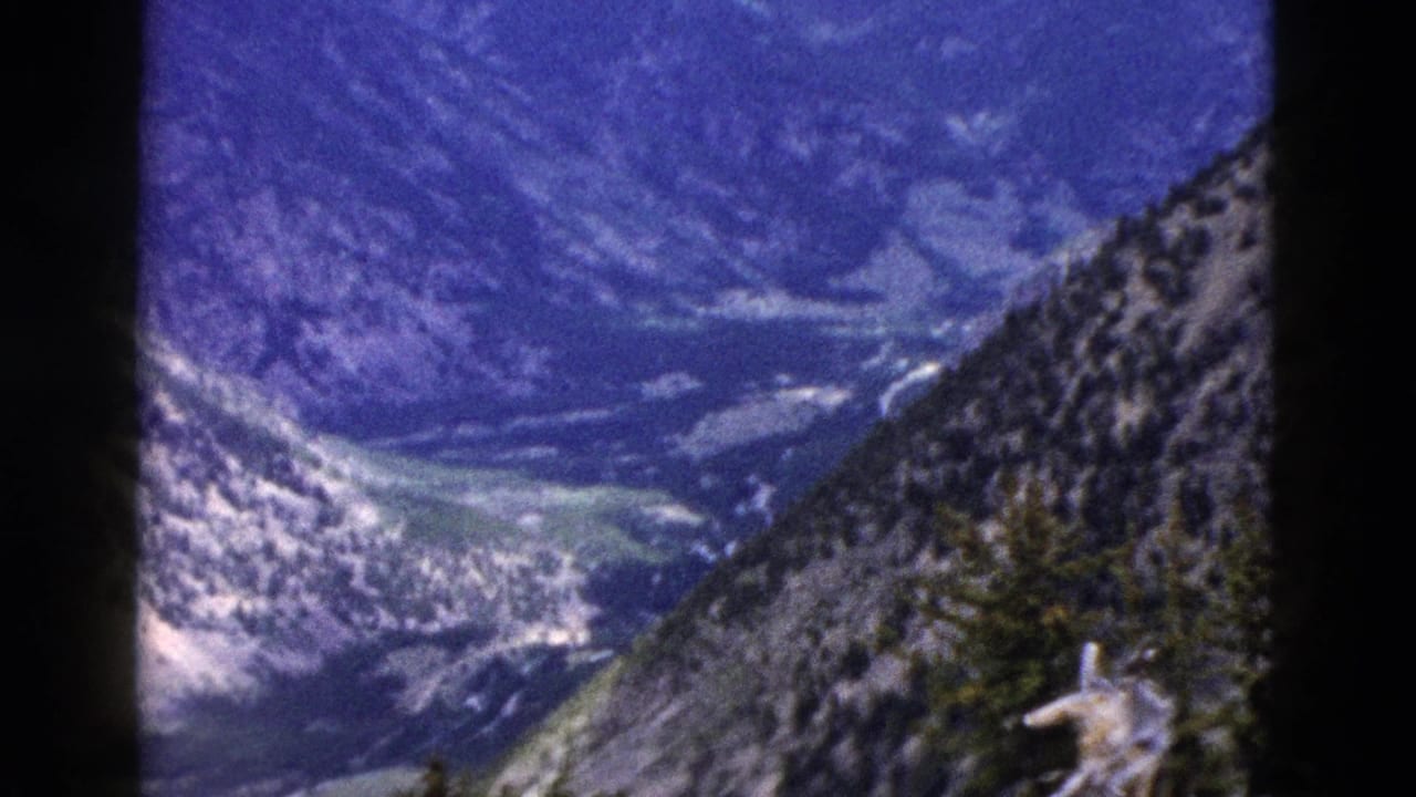 1958 8mm Yellowstone home-movie frame showing a high overlook toward a mountain valley with rocky slopes and forested ridges.