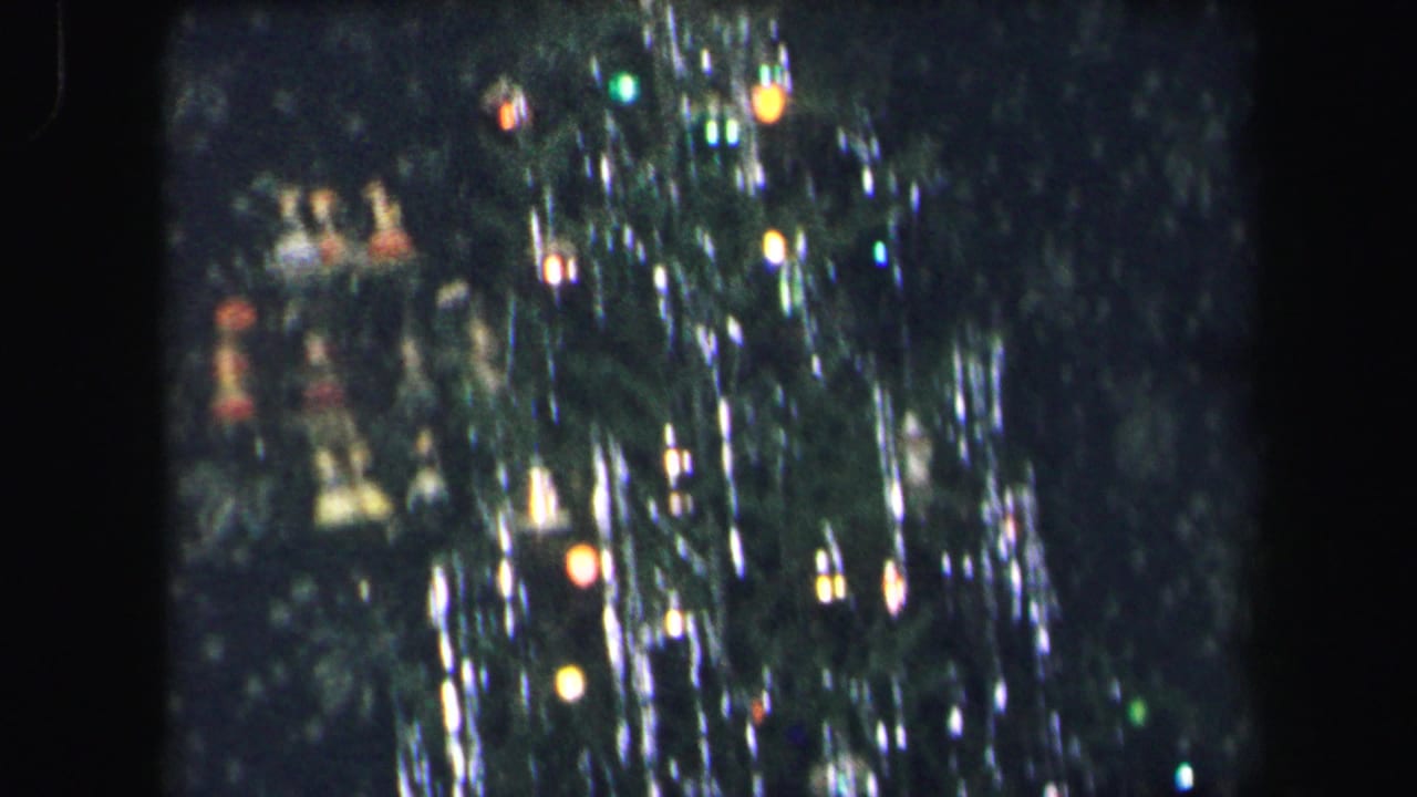 Decorated Christmas tree with colored lights and reflective tinsel in a dark interior.