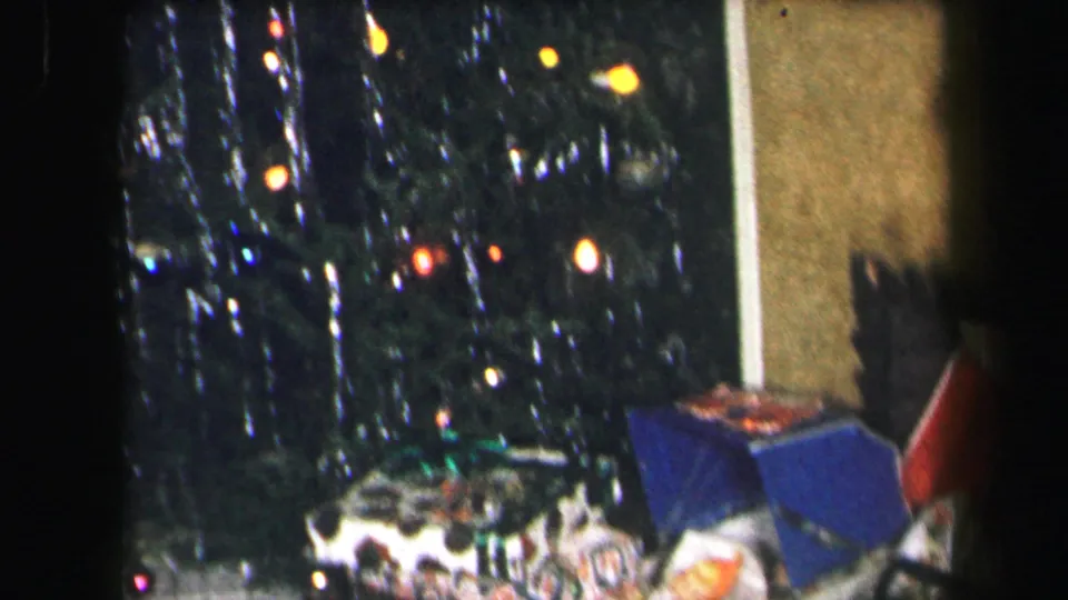 1971 Lynbrook holiday frame with a lit tree above a cluster of wrapped gifts and toys on the floor.