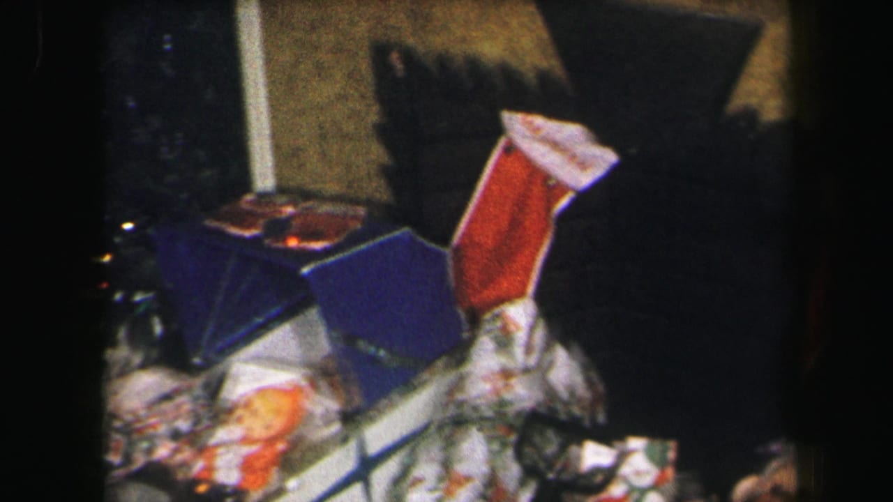 Wrapped gifts and a red-hooded doll arranged on a table in a dim indoor room.